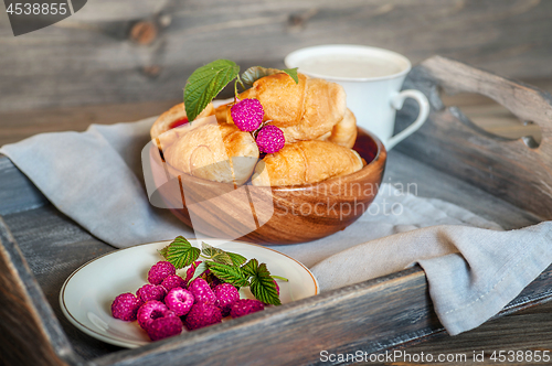 Image of Croissants with raspberries on a wooden tray. The concept of a wholesome breakfast.