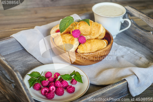 Image of Croissants with raspberries on a wooden tray. The concept of a wholesome breakfast.