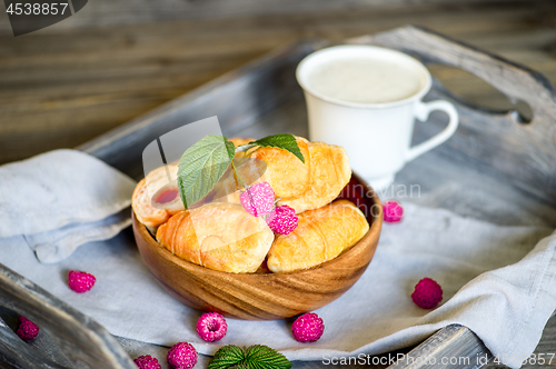 Image of Croissants with raspberries on a wooden tray. The concept of a wholesome breakfast.