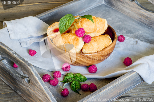 Image of Croissants with raspberries on a wooden tray. The concept of a wholesome breakfast.