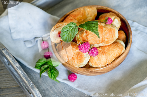 Image of Croissants with raspberries on a wooden tray. The concept of a wholesome breakfast.