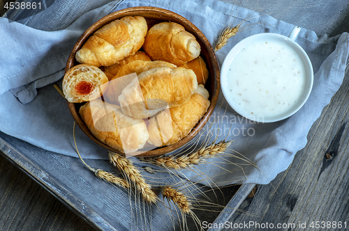 Image of Croissants, a cup with kefir and ears of grain on a wooden tray. The concept of a wholesome breakfast.