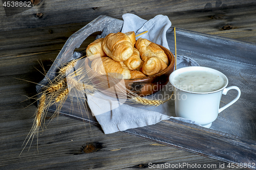 Image of Croissants, a cup with kefir and ears of grain on a wooden tray. The concept of a wholesome breakfast.