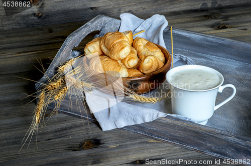 Image of Croissants, a cup with kefir and ears of grain on a wooden tray. The concept of a wholesome breakfast.