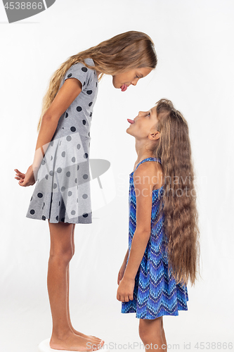 Image of A girl stands on a chair, another girl stands nearby, show each other tongues