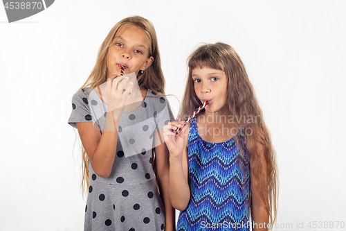 Image of Two girls suck lollipops and look in the frame