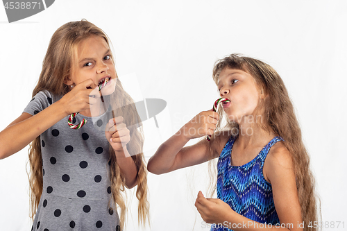 Image of Two girls eagerly bite and suck caramel candies