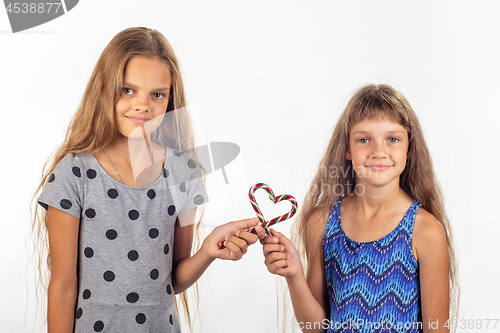 Image of Two girls made a heart out of two lollipops and look into the frame