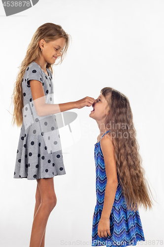 Image of Two girls of different stature, one stood on a chair and pulls the other girl by the nose