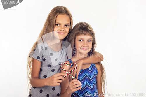 Image of Two girls hugging made a heart out of two lollipops