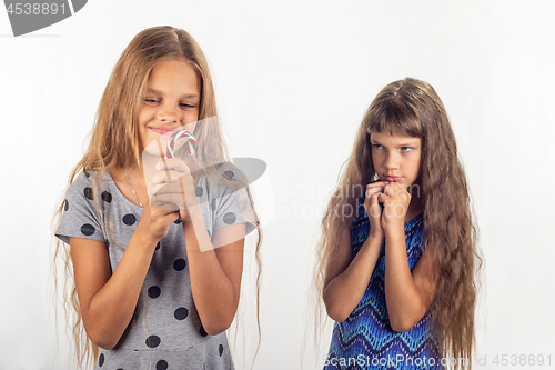 Image of One girl has a lollipop in her hands, the other behind her looks at the girl reproachfully