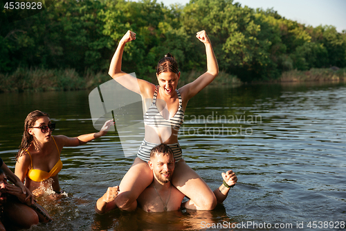 Image of Happy group of friends having fun, laughting and swimming in river