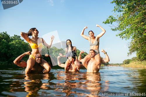 Image of Happy group of friends having fun, laughting and swimming in river