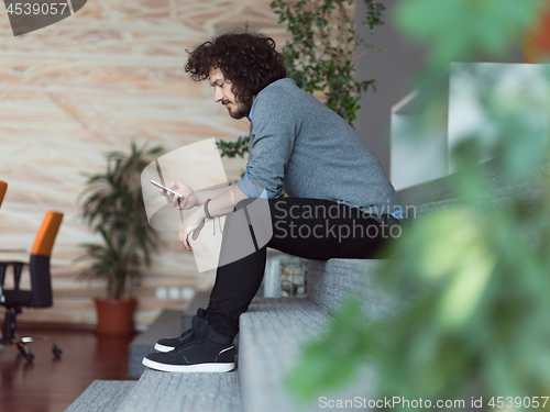 Image of Young casual businessman holding smartphone