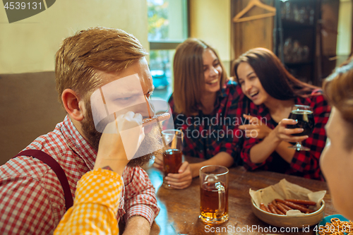 Image of people, leisure, friendship and communication concept - happy friends drinking beer, talking and clinking glasses at bar or pub