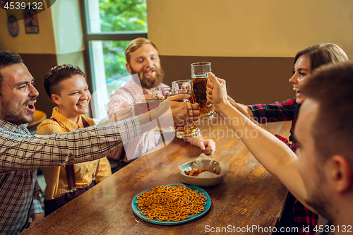 Image of people, leisure, friendship and communication concept - happy friends drinking beer, talking and clinking glasses at bar or pub