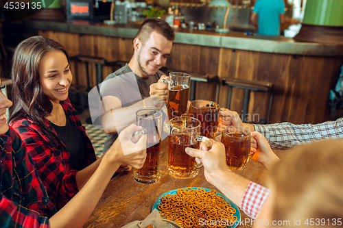 Image of people, leisure, friendship and communication concept - happy friends drinking beer, talking and clinking glasses at bar or pub