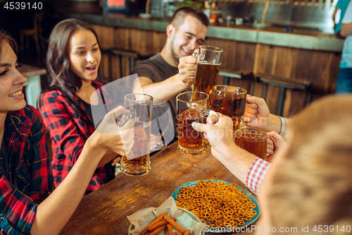 Image of people, leisure, friendship and communication concept - happy friends drinking beer, talking and clinking glasses at bar or pub