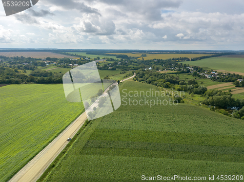 Image of Bird\'s eye view from drone to a rural landscape with a village, dirt road and agricultural fields of planted crops at cloude background.