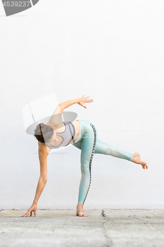 Image of Fit sporty active girl in fashion sportswear doing yoga fitness exercise in front of gray wall, outdoor sports, urban style