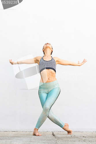 Image of Fit sporty active girl in fashion sportswear doing yoga fitness exercise in front of gray wall, outdoor sports, urban style