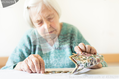 Image of Concerned elderly woman sitting at the table counting money in her wallet.