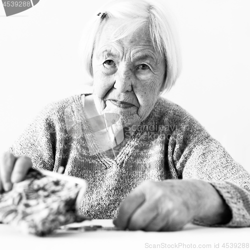 Image of Concerned elderly woman sitting at the table counting money in her wallet. Black and white photo.