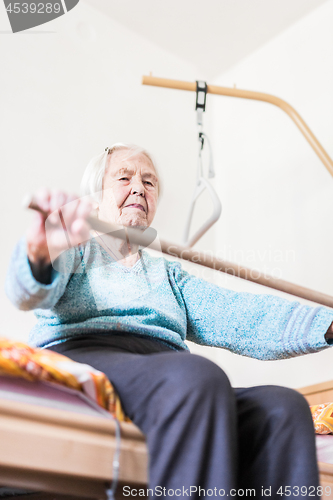 Image of Elderly 96 years old woman exercising with a stick sitting on her bad.