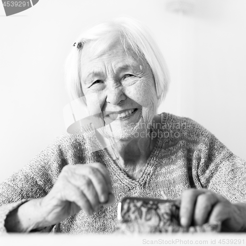 Image of Cheerful elderly 96 years old woman sitting at table at home happy with her pension savings in her wallet after paying bills. Black and white.