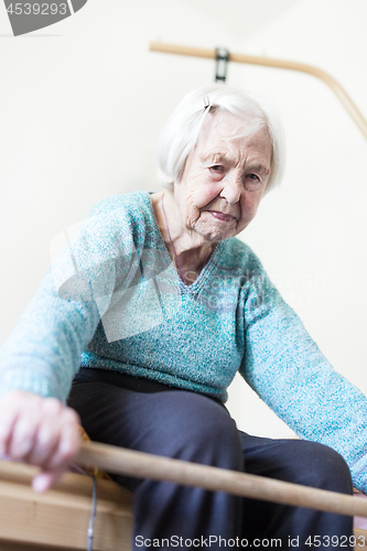 Image of Elderly 96 years old woman exercising with a stick sitting on her bad.