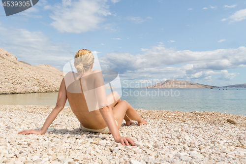 Image of Rear view of sexy young caucasian woman sunbathing topless on romote pabble beach on Pag island, Croatia, Mediterranean.