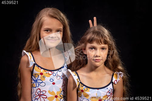 Image of The older sister put the little horns, a portrait on a black background