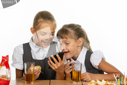 Image of Two schoolgirls at a break watching a video on the phone, and eating liver and orange, drinking juice