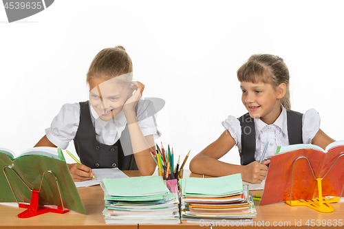 Image of Two schoolgirls are sitting at a desk and cheerfully looking at the textbook