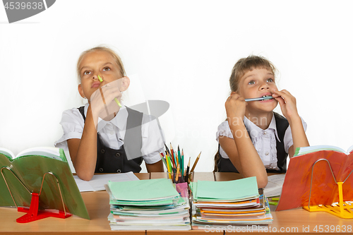 Image of Two schoolgirls pensively and funny sit at the table and look up