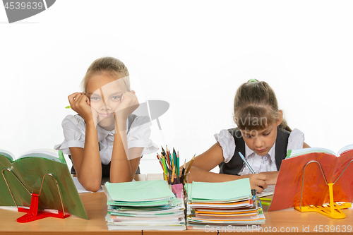 Image of Two schoolgirls at a desk, one leaning on her hands and looking into the frame, the other writes