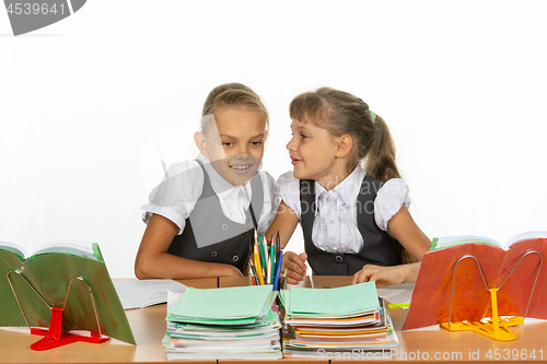 Image of Two girls whisper while sitting at a desk