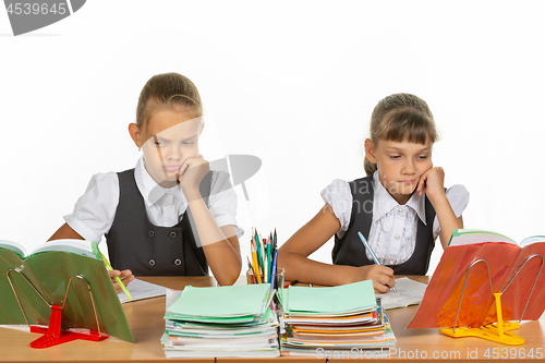 Image of Sad schoolgirls look at a book in a lesson