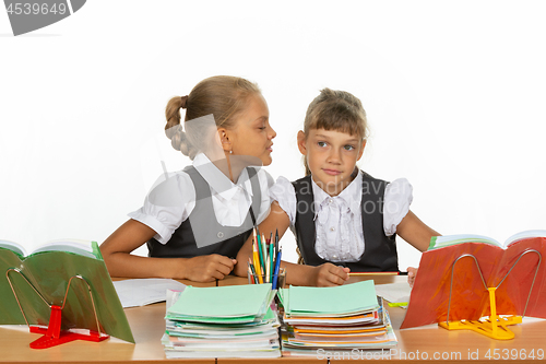 Image of Girls are sitting at a school desk, one whispers to the other something in the ear