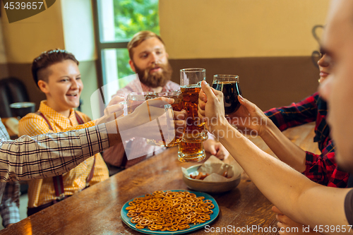 Image of people, leisure, friendship and communication concept - happy friends drinking beer, talking and clinking glasses at bar or pub