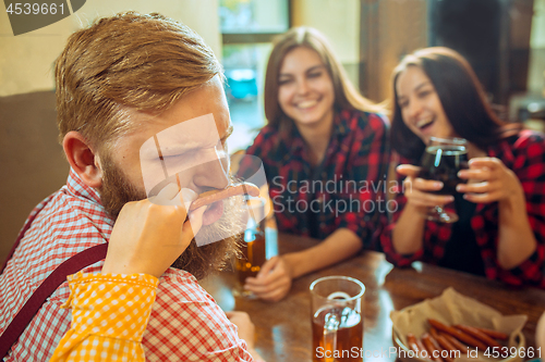 Image of people, leisure, friendship and communication concept - happy friends drinking beer, talking and clinking glasses at bar or pub