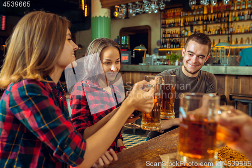 Image of people, leisure, friendship and communication concept - happy friends drinking beer, talking and clinking glasses at bar or pub