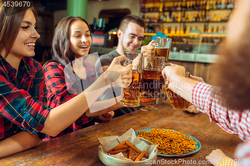 Image of people, leisure, friendship and communication concept - happy friends drinking beer, talking and clinking glasses at bar or pub