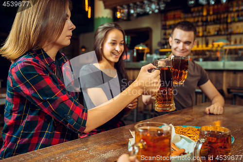 Image of people, leisure, friendship and communication concept - happy friends drinking beer, talking and clinking glasses at bar or pub