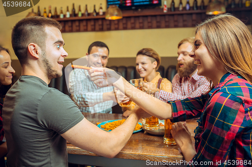 Image of people, leisure, friendship and communication concept - happy friends drinking beer, talking and clinking glasses at bar or pub