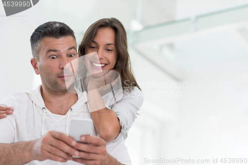 Image of happy couple using mobile phone at home