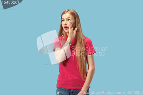 Image of The young woman whispering a secret behind her hand over blue background