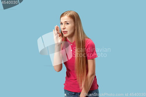 Image of The young woman whispering a secret behind her hand over blue background