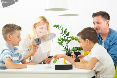 Image of Happy young family playing card game at dining table at bright modern home.