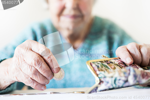 Image of Detailed closeup photo of unrecognizable elderly womans hands counting remaining coins from pension in her wallet after paying bills.